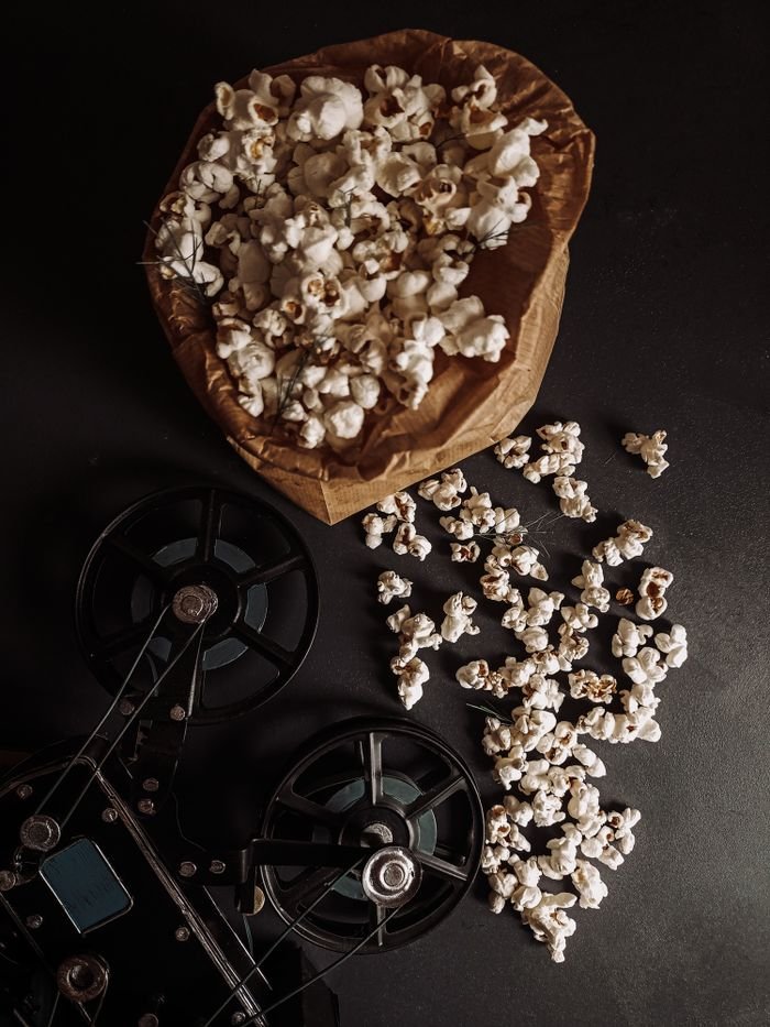 Top view of popcorn in a paper bag with vintage film reels on a dark surface.